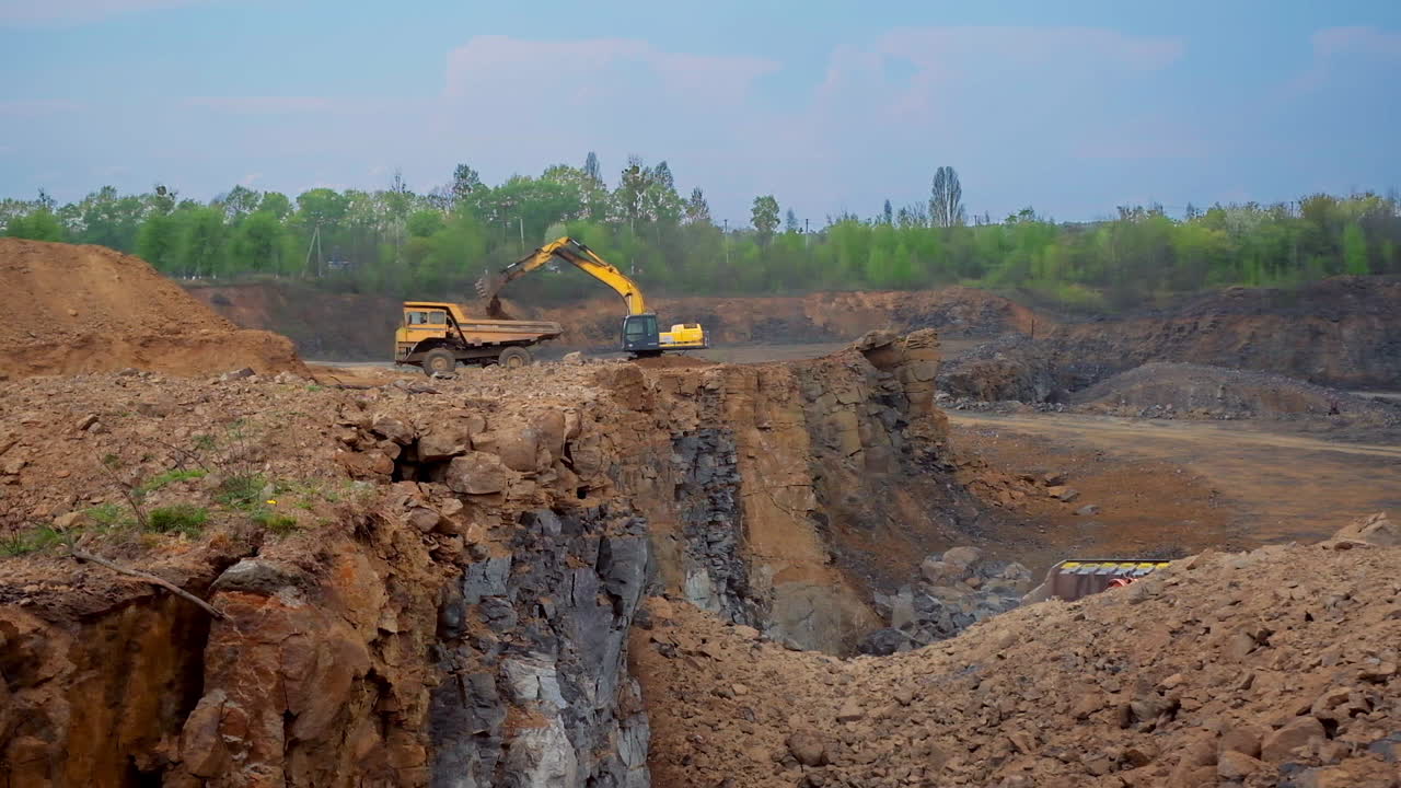 Tractor bucket is filling a truck. Industrial excavator loading soil on a truck on nature background. Earth moving equipment.