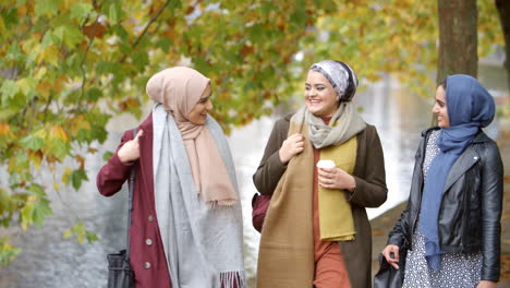 british muslim female friends walking by river in city