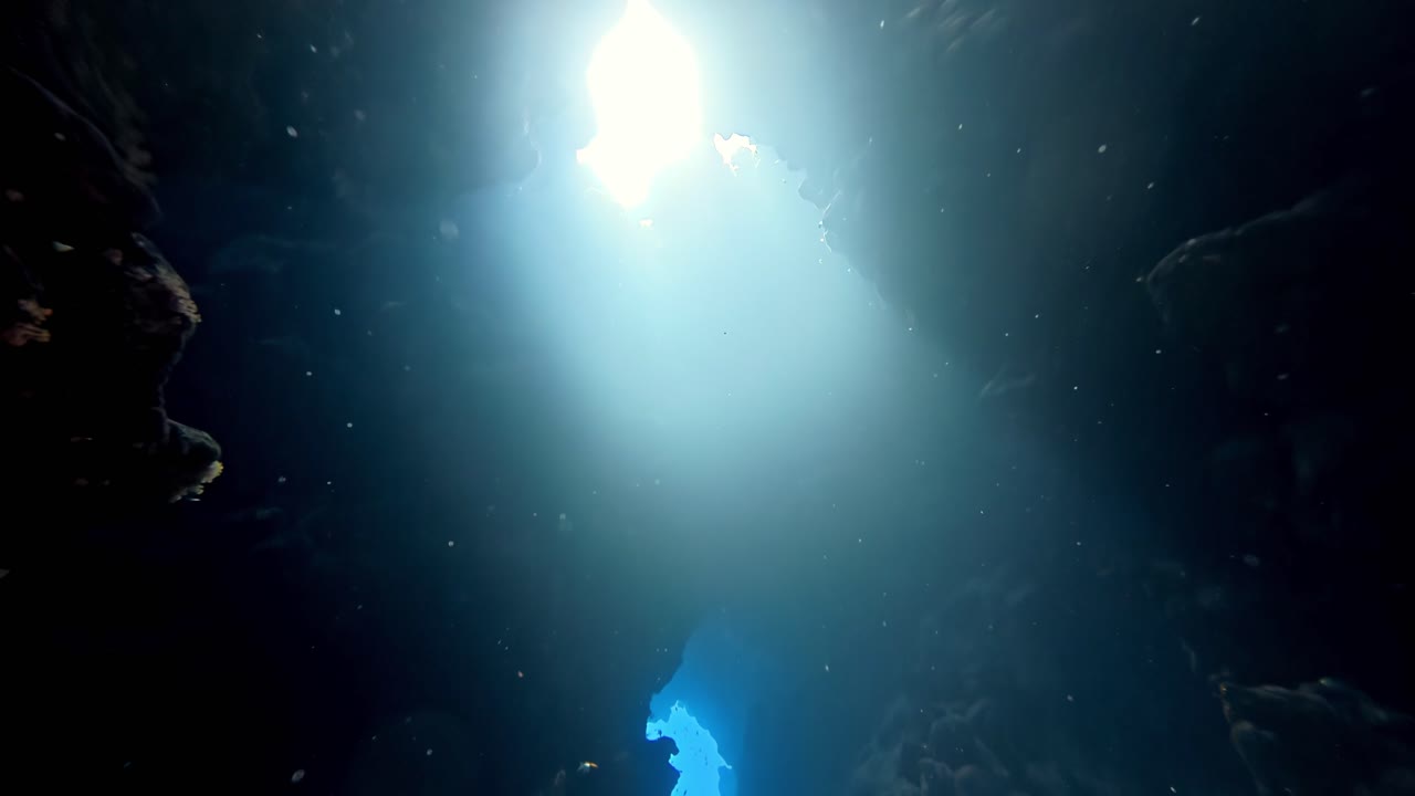 Exploração atmosférica de cavernas subaquáticas com feixes de luz solar etéreos perfurando as águas escuras e profundas do oceano, em uma vista dramática de baixo ângulo capturando o brilho do solstício de verão e silhuetas aquamarinas azuis e sombrias