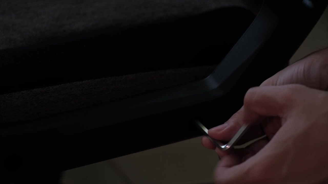 Primer plano de manos usando una llave Allen para ajustar un componente de una silla gaming durante el montaje de muebles de interior.