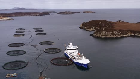 drone shot circling a fish farming well-boat anchored to a fish cage