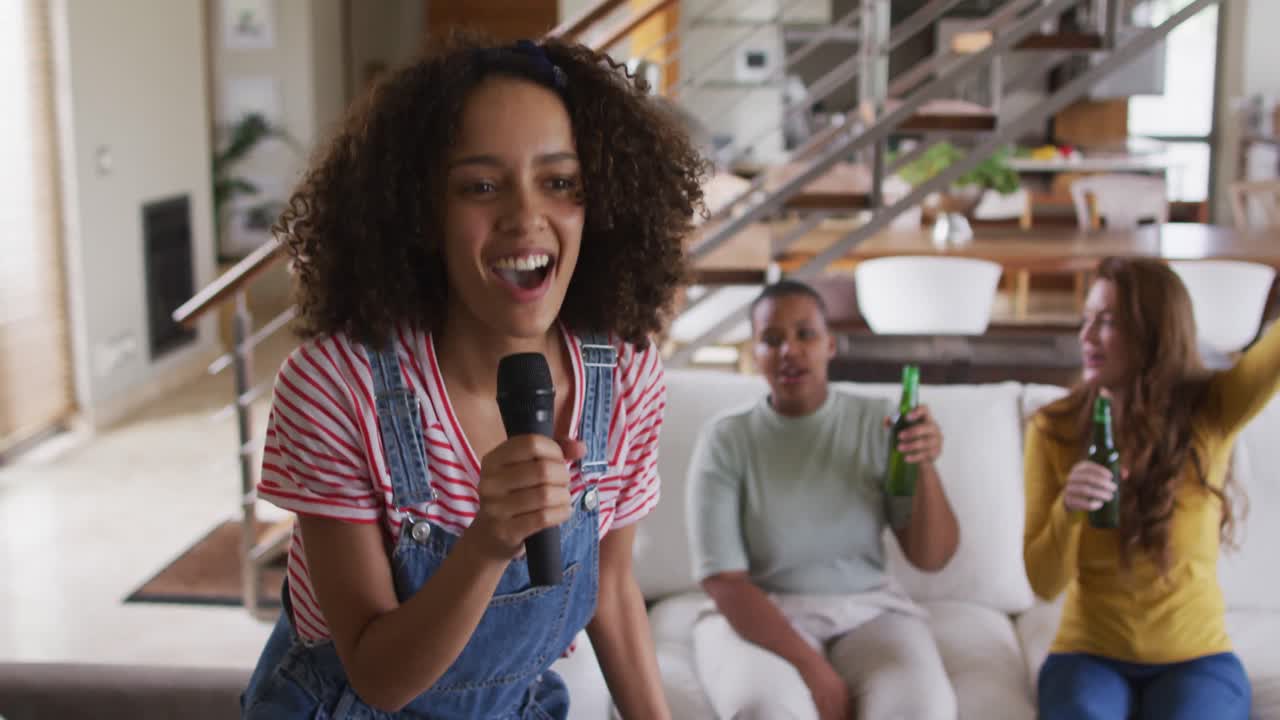 Diverse group of female friends having fun singing karaoke and drinking beer at home