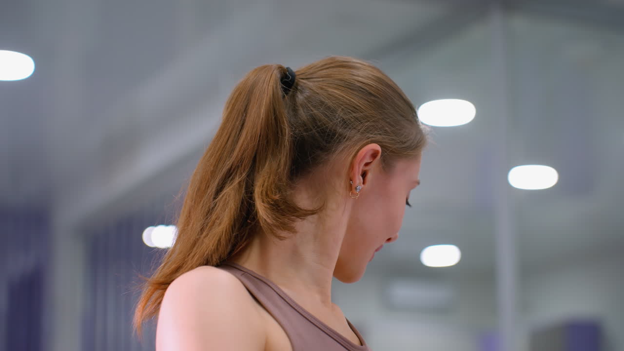 젊은 여성의 클로즈업, 깊은 스트레치 운동에서 무에 손을 고, 부드러운 보케 천장 조명과 함께, 조용한 피트니스 환경에서 자세, 유연성 및 튼튼한 신체에 초점을 맞추십시오.