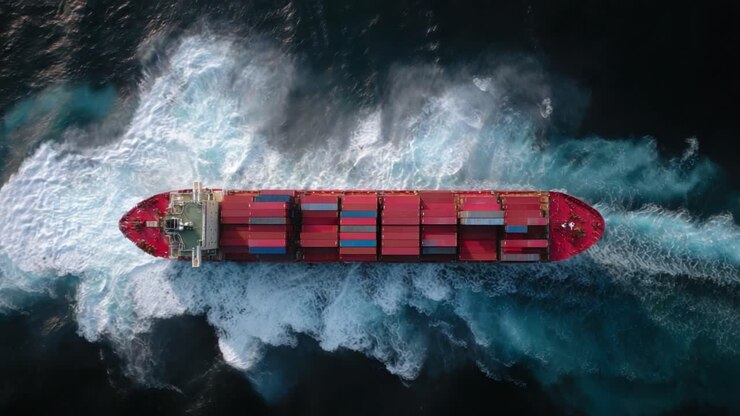 An Aerial View of a Large Cargo Ship Navigating Through the Ocean, Leaving a Trail of Wake and Splashing Water Behind, Showcasing Its Container Stack and Maritime Journey
