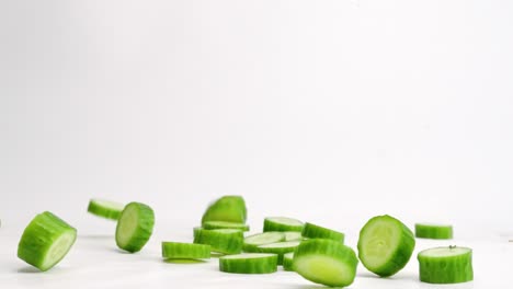 Persian-mini-cucumber-slices-falling-onto-white-table-top-and-bouncing-into-a-pile-in-slow-motion