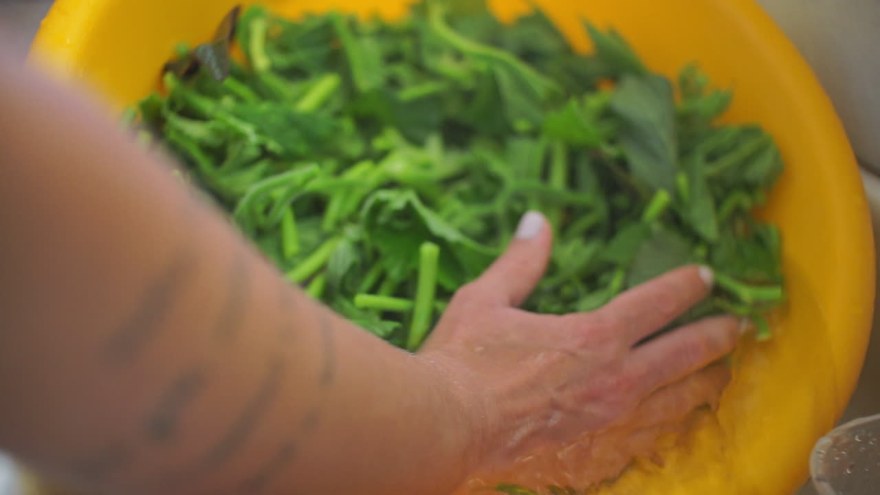 여자는 집에 있는 노란색 플라스틱 분지에서 채소를 씻는다