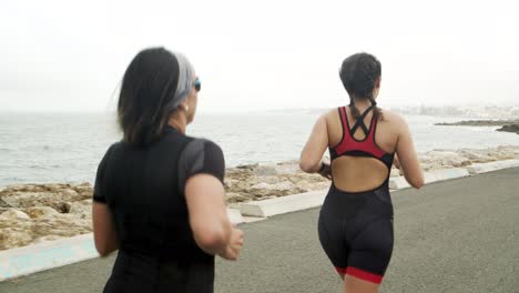 vista trasera de triatletas femeninas entrenando para maratón en una carretera cerca del mar