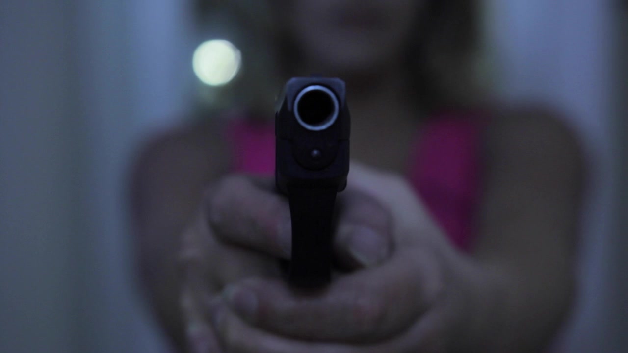 Young Woman pointing a gun at the target hallway in background, selective focus on front of gun