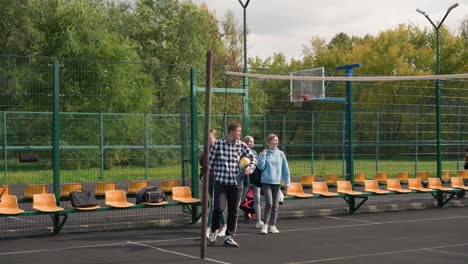 group of young volleyball players with coach in outdoor court, looking around and preparing for warm-up run, wearing casual sports attire amidst vibrant green backdrop