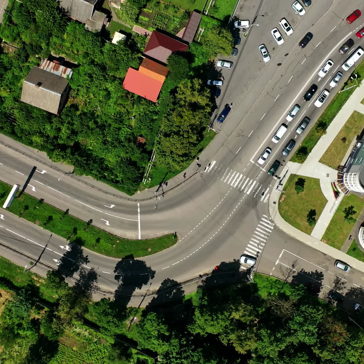 Cars driving on road. Traffic movement among green trees and modern buildings in the city. Panoramic shot of the city highway. Top view.
