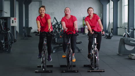 healthy caucasian group of women exercising workout on stationary cycling machine bike in gym