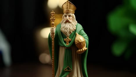 close up of a saint patrick figurine, adorned in a green and white robe and mitre, holding a golden crosier against a softly blurred backdrop of green leaves and warm lights