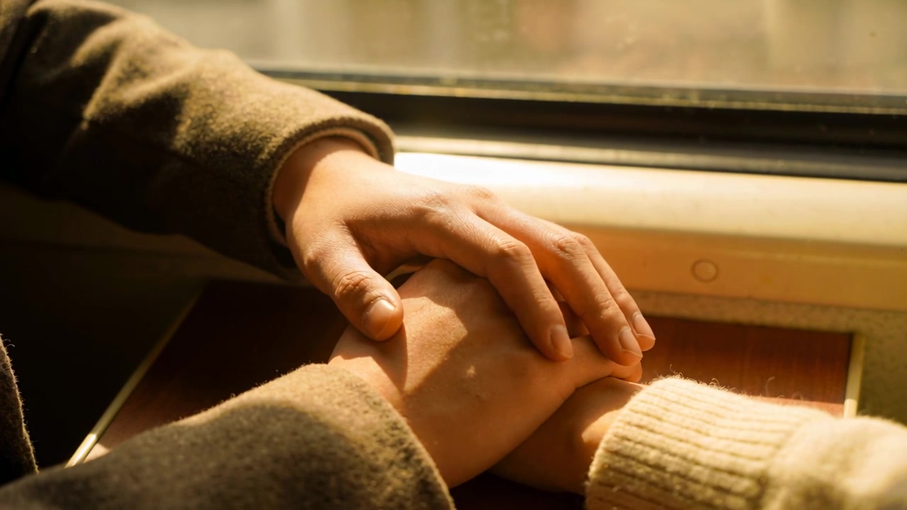 Resting man's hand over hers on train tray, sun warming coat sleeve, knit sleeve, comforting