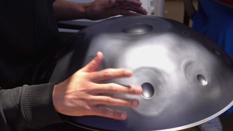 close-up of a mans hand playing on modern musical instrument hand pan or vadjraghanta or metal tongue drumon, selective focus