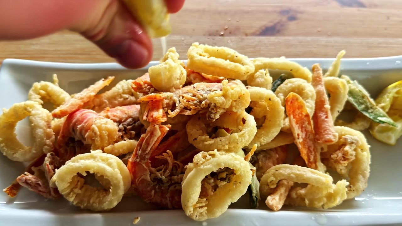 Close-up de Clássico Fritto Misto Italiano com Lula, Camarão e Vegetais Fritos Sendo Espremido com Limão Fresco Perto do Lago Iseo Celebrando a Culinária Tradicional de Frutos do Mar.