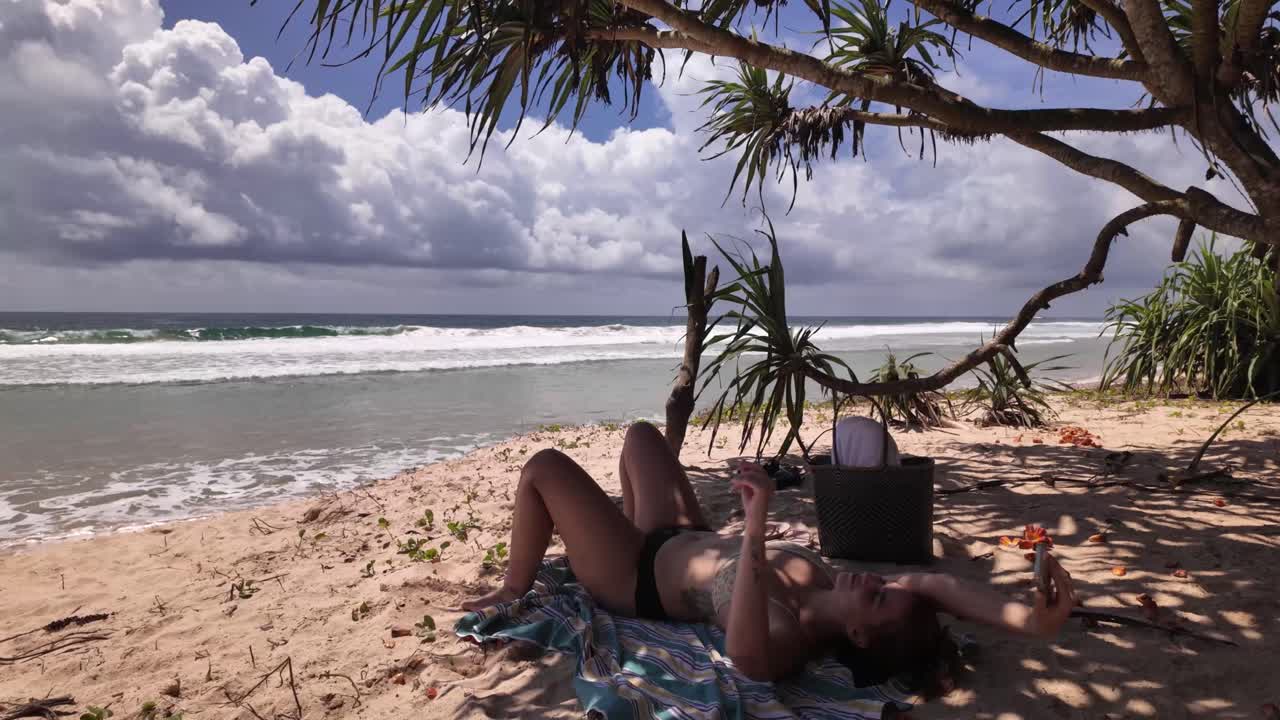 Beautiful young woman in holiday, sand lounging under palm tree shade bikini beachwear