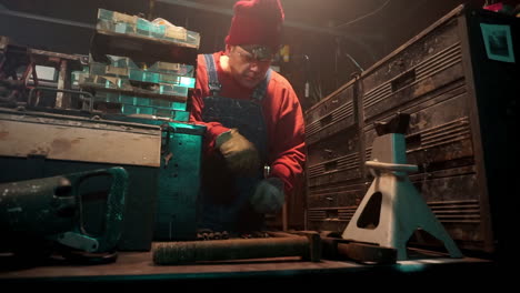 workman puts on gloves and picks up a pipe wrench from a workbench