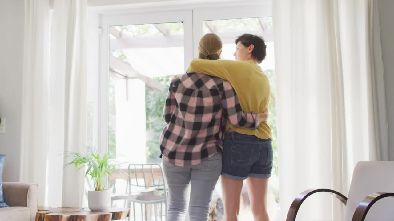 Two mid adult women embracing at glass door, animated emojis rising from floor for social marketing