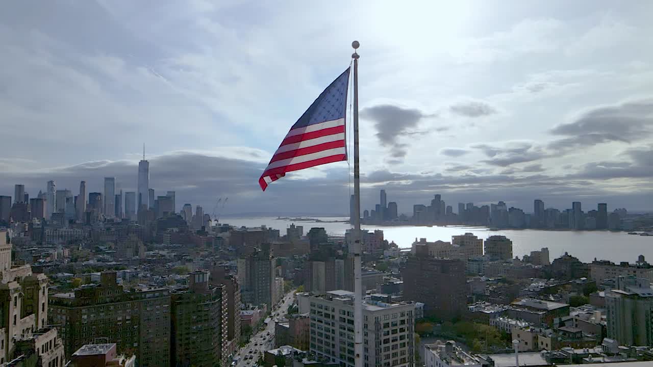Ripresa aerea al rallentatore della bandiera degli USA che sventola al vento con New York City sullo sfondo