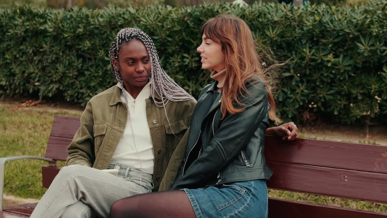 Two Young Women Relaxing and Chatting on a Bench in a Park