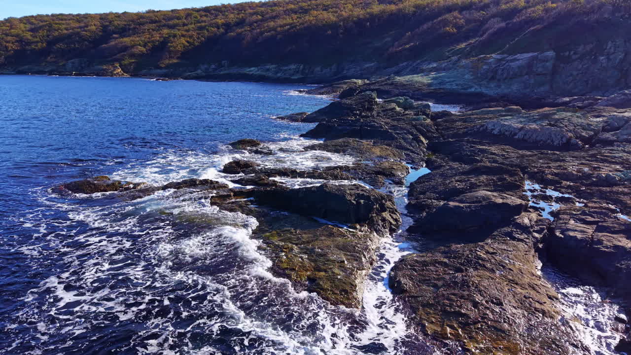 Ondas acariciam suavemente a costa rochosa em um local costeiro tranquilo sob um céu azul claro durante uma tarde ensolarada