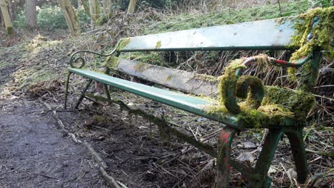 Moosig-Bewachsener-Alter-Verwitterter-Grüner-Gewellter-Schmiedeeiserner-Holzsitz,-Der-Im-Wald-Aufgegeben-Wurde