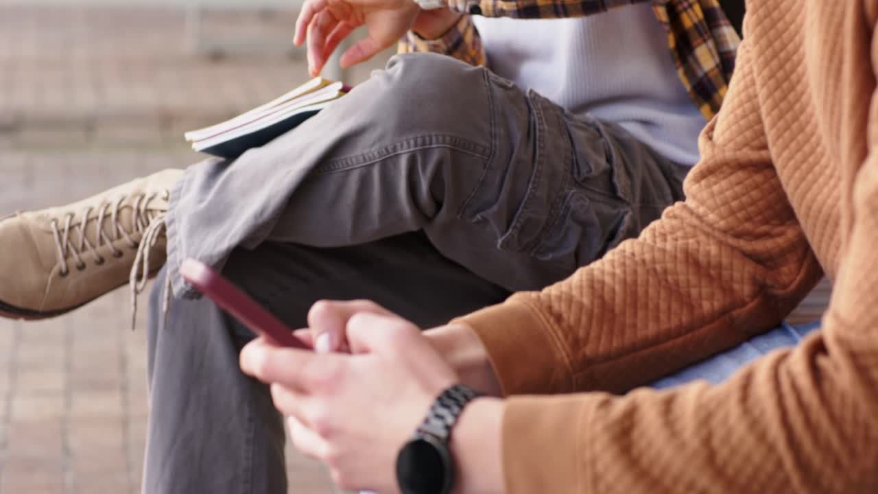 Due amici seduti su una panchina in piazza che guardano l'ora sullo smartwatch e scorrono lo smartphone