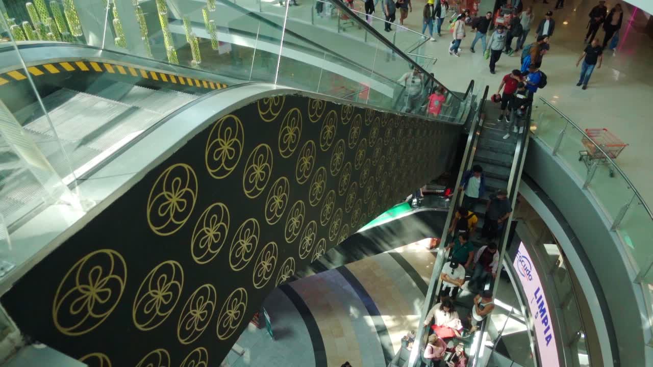 Shoppers move up an escalator in a modern mall with decorative panels and bright lighting