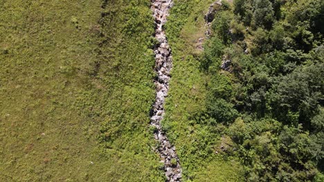 Wasser-Fließt-Aus-Dem-Bogen-Zwischen-Den-Bergen,-Blick-Auf-Den-Bach-Von-Oben