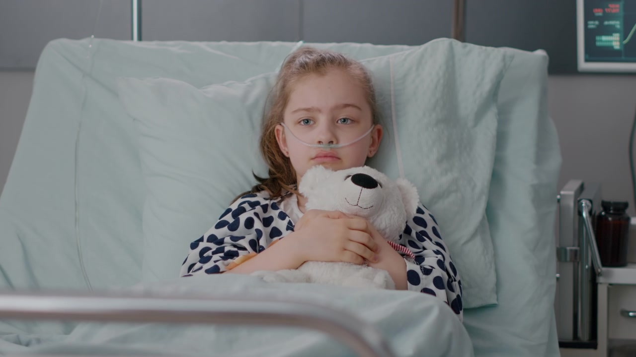 Sad Young Girl With Teddy Bear Sitting in Hospital Bed