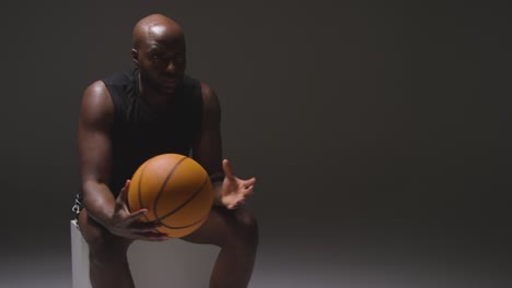 studio shot of seated male basketball player with hands holding ball