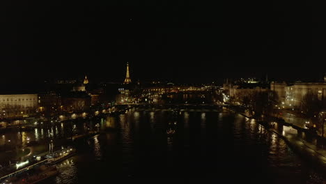 Aerial-footage-of-night-city.-Seine-river-water-surface-reflecting-lights.-Illuminated-Eiffel-Tower-in-distance.-Paris,-France