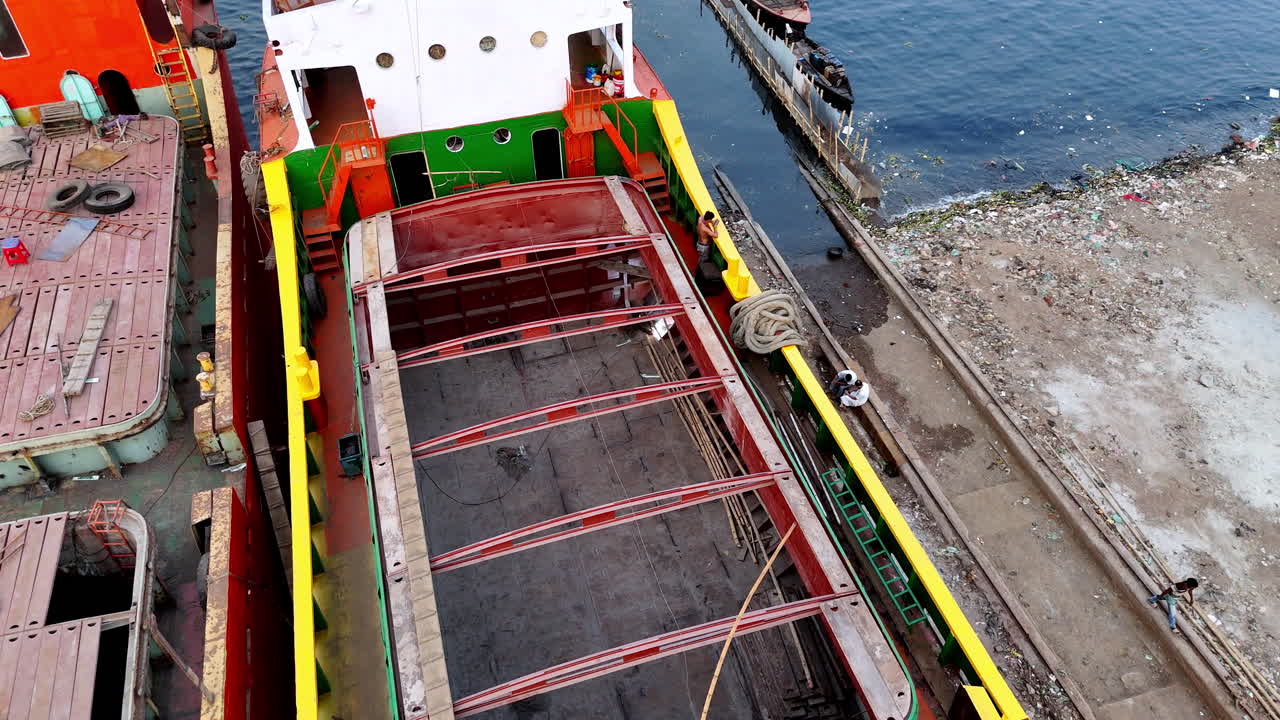 Cinematic aerial drone shot focusing on a welder working on a cargo ship docked along the Buriganga river in Dhaka, Bangladesh.
