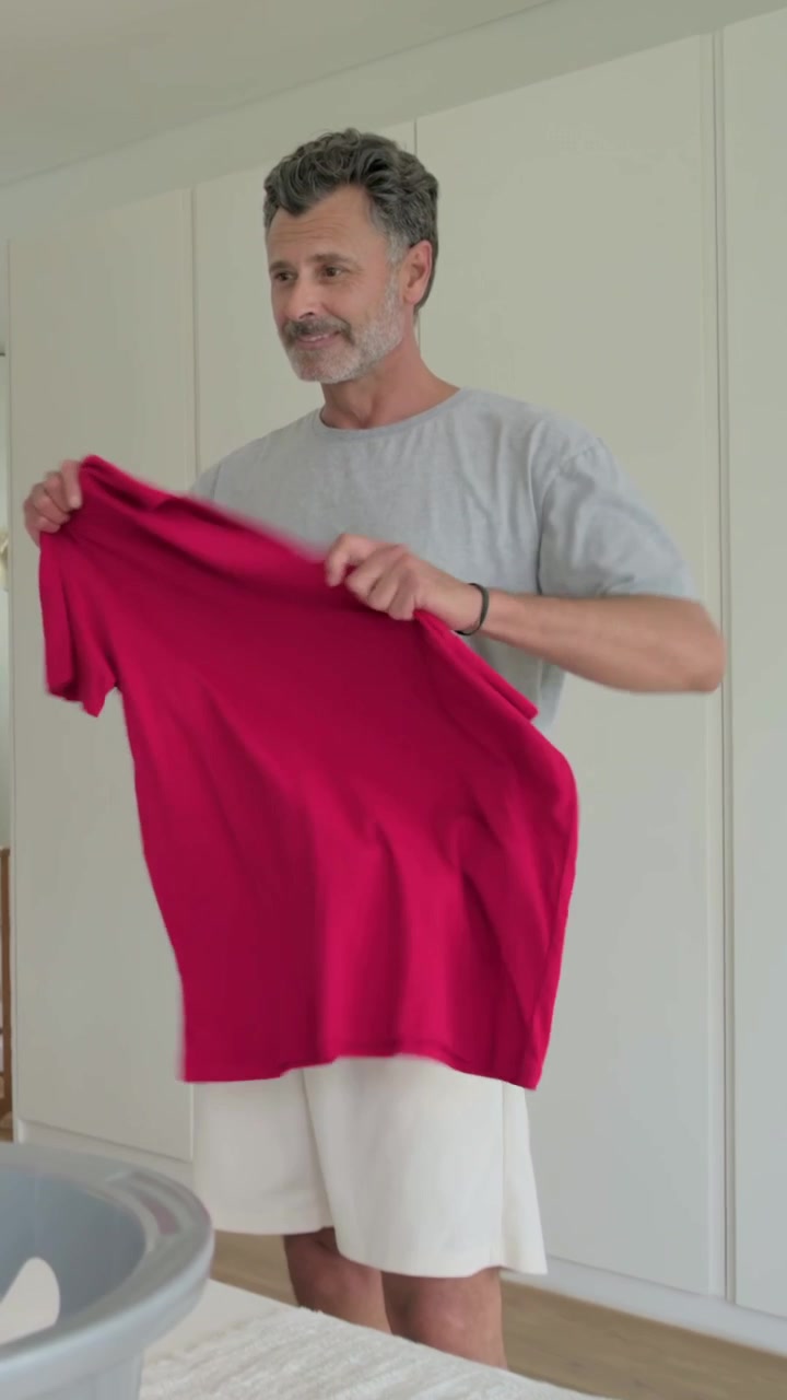 Vertical video: Seeing grey basket, man in tee pulling red shirt folding placing on bed to store