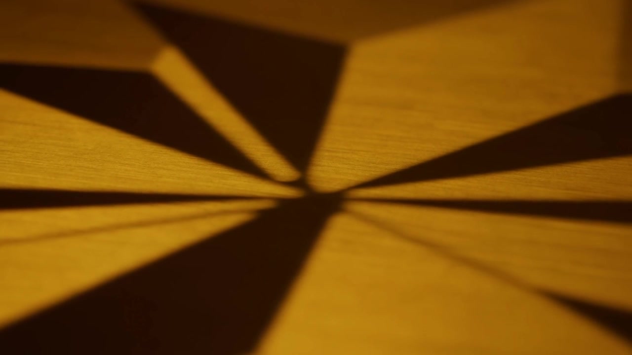 Een centraal schaduwpatroon verschuift op een houten tafelblad, met een verschuivende lamp en gevouwen papieren randen.