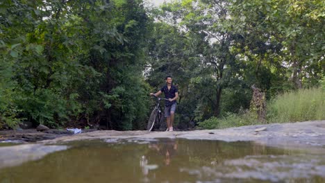 boy man carring bycycle through rockes in jungle wide shot