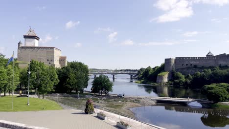 border between estonia and russia in summer 2022 - establishing shot with two castles along the river of narva connected by a road bridge