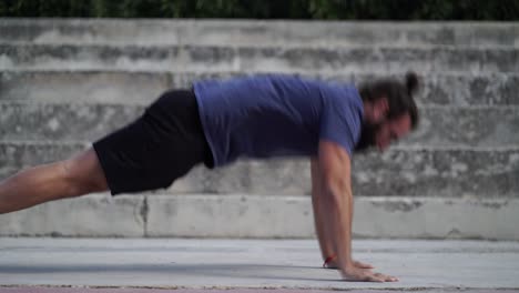 Bearded-man-trains-his-strength-by-doing-push-ups-with-a-clap-on-the-ground-outdoors-during-daylight