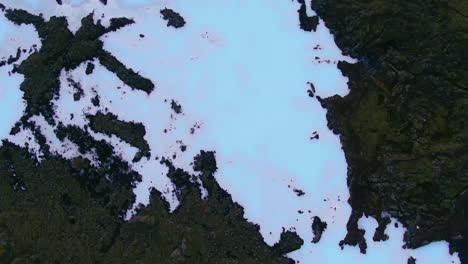 Breathtaking-aerial-top-down-spin-2-view-of-a-blue-lagoon-snow-and-ice-covered-rocky-terrain-in-Iceland