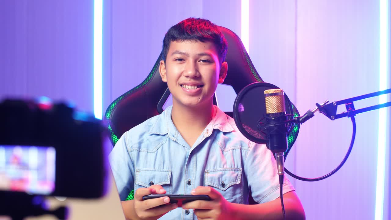 Excited Asian Kid Boy Playing Video Game With Mobile Phone Then Smiles To Camera While Live Stream