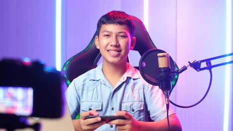 excited asian kid boy playing video game with mobile phone then smiles to camera while live stream