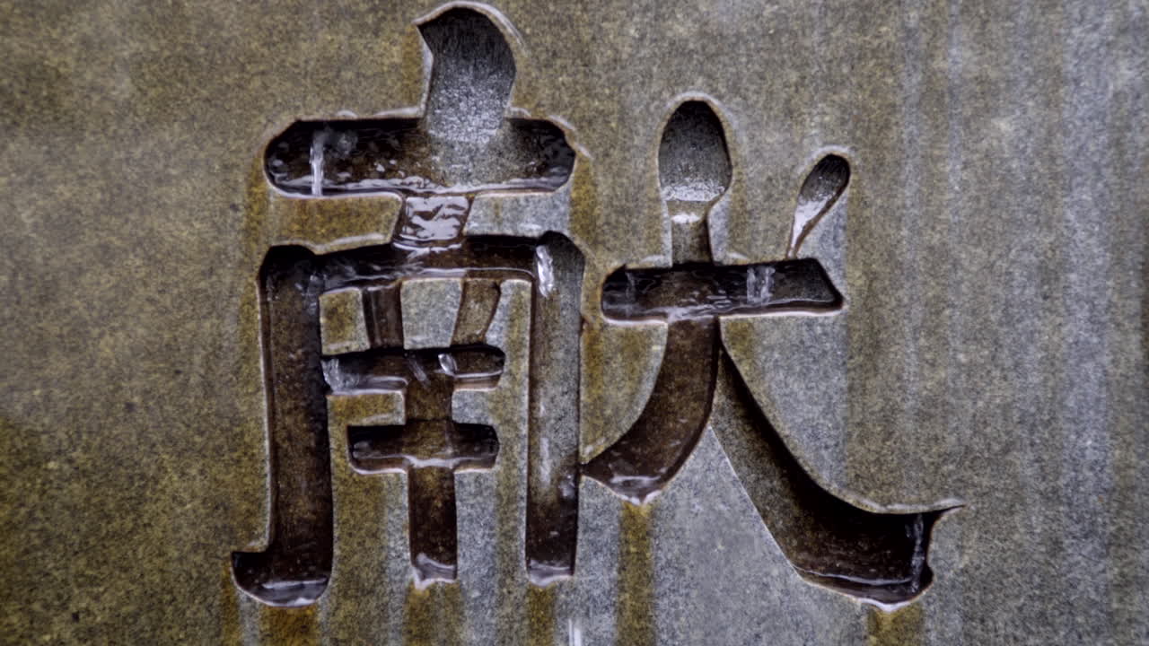 Water flowing over Japanese kanji symbol etched in stone, close up