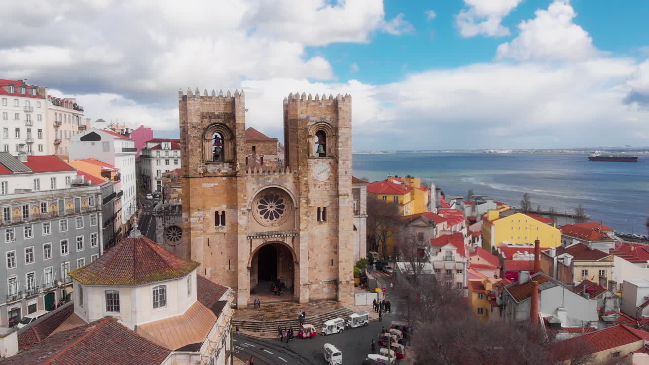 Cattedrale di Lisbona Sé de Lisboa visibile sopra i tetti storici con il fiume Tago e un traghetto sullo sfondo.