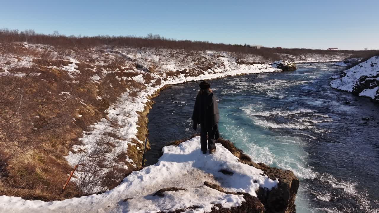 Woman stands by icy Brúarfoss river in Laugarvatn Iceland winter landscape