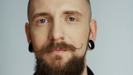 portrait of the smiled good looking hipster man with earings smiling and looking straight to the camera on the white wall background