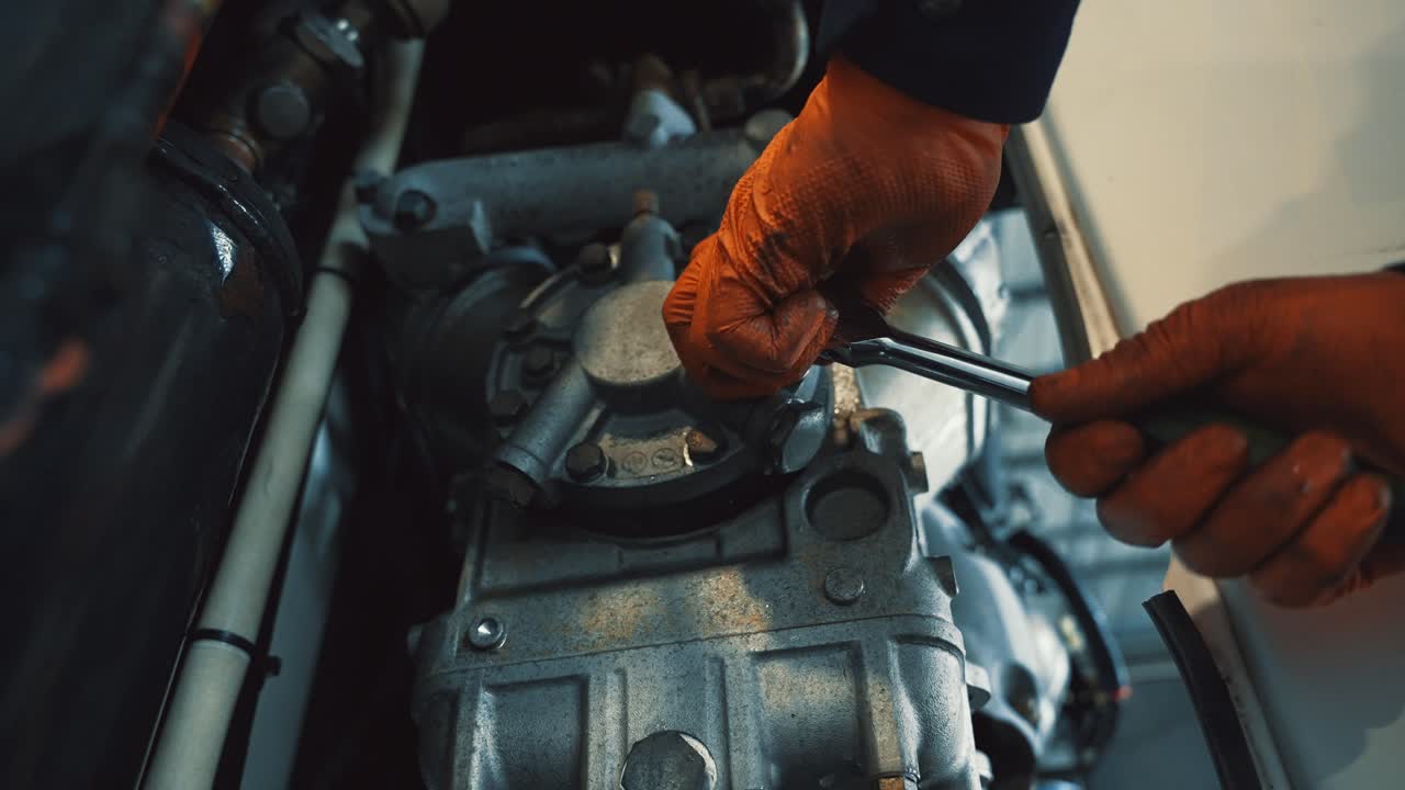 mecánico con guantes naranjas ata los pernos con una llave inglesa de una cubierta de un motor pequeño