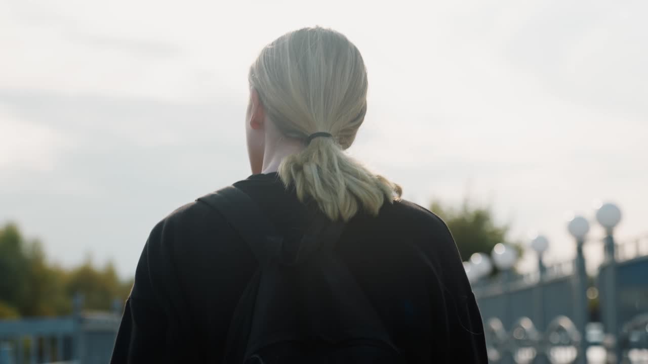Man on bridge gazes outward. Urban scene featuring reflective man overlooking horizon at dusk. Solitary man with backpack and ponytail contemplates horizon during sunset on city bridge