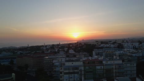 Vista-Aérea-De-La-Puesta-De-Sol-Sobre-Lisboa,-Situada-En-El-Lejano-Puerto-Deportivo.