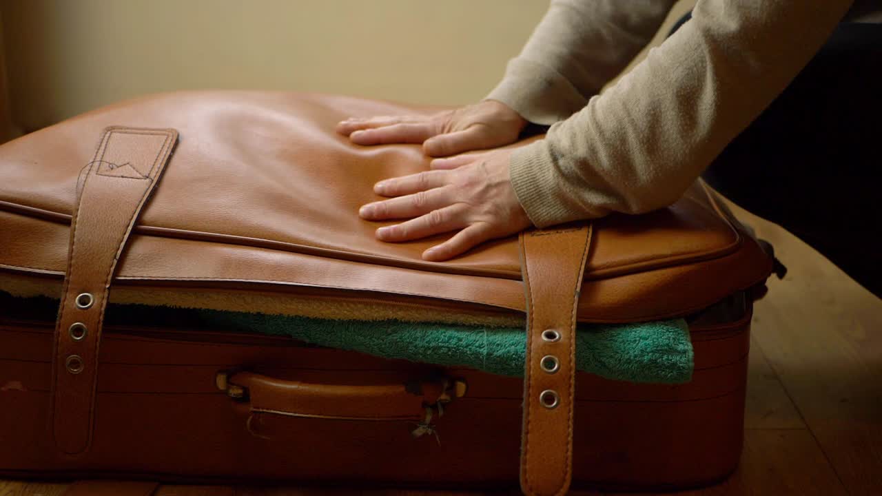 Hand trying to close stuffed over filled suitcase close up shot