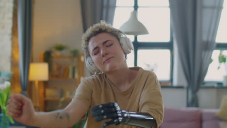 chica con brazo protésico en auriculares inalámbricos bailando en casa